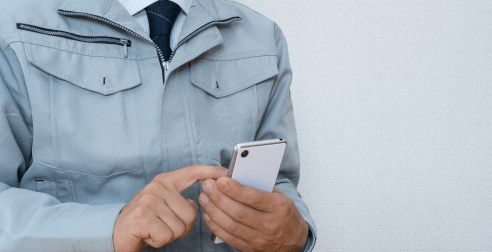 作業着姿の男性がスマートフォンを操作している様子